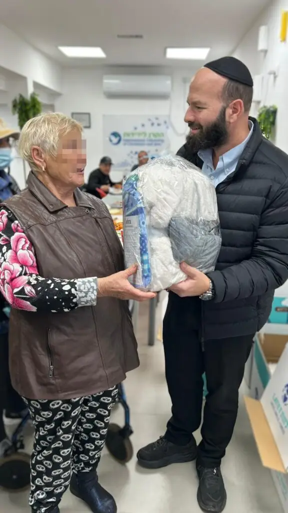 אישה מבוגרת מקבלת שמיכת פוך מחממת לחורף במסגרת פעילות סיוע של מפעל החסד יד ביד