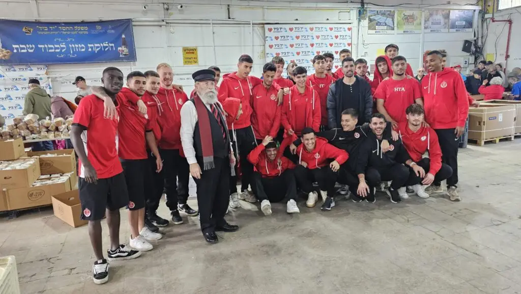 Hapoel Tel Aviv youth team volunteering with Yad B’Yad – Factory of Kindness in Lod, helping prepare and distribute food baskets to families and seniors in need.
